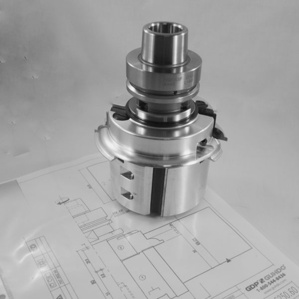 A precision-machined metallic industrial component with a cylindrical body featuring multiple threaded sections, stepped diameters, and machined grooves, positioned on a technical drawing or blueprint background with grid lines visible.