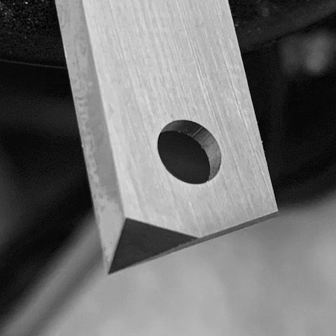 Machined metal rectangular component with cylindrical drilled hole showing manufacturing marks and precision metalworking