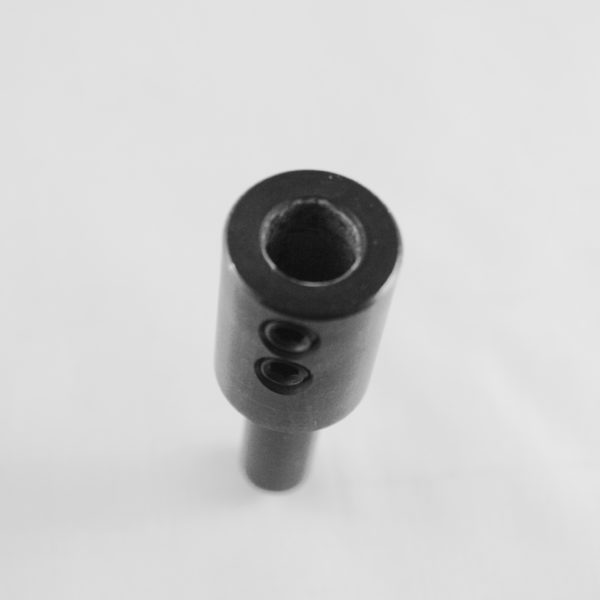 Black and white photograph of a metallic cylindrical mechanical component viewed from above, showing a central bore hole and two smaller holes on the side surface, with a smaller diameter shaft extending from the bottom. The part appears to be a coupling or connector piece against a light gray background.