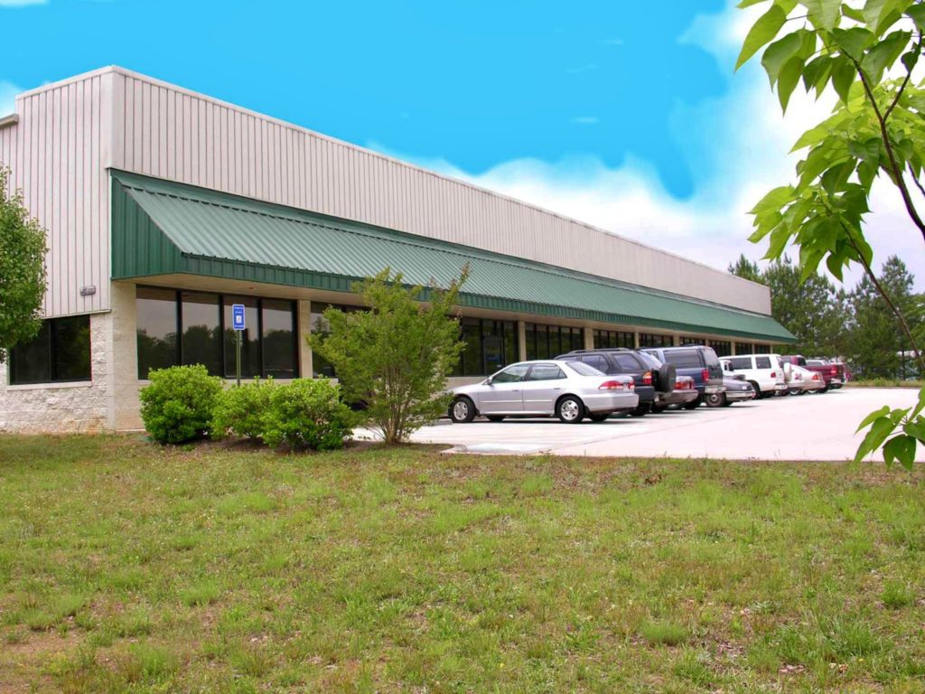Commercial office building with metal roof, parking lot, and landscaping in suburban business park